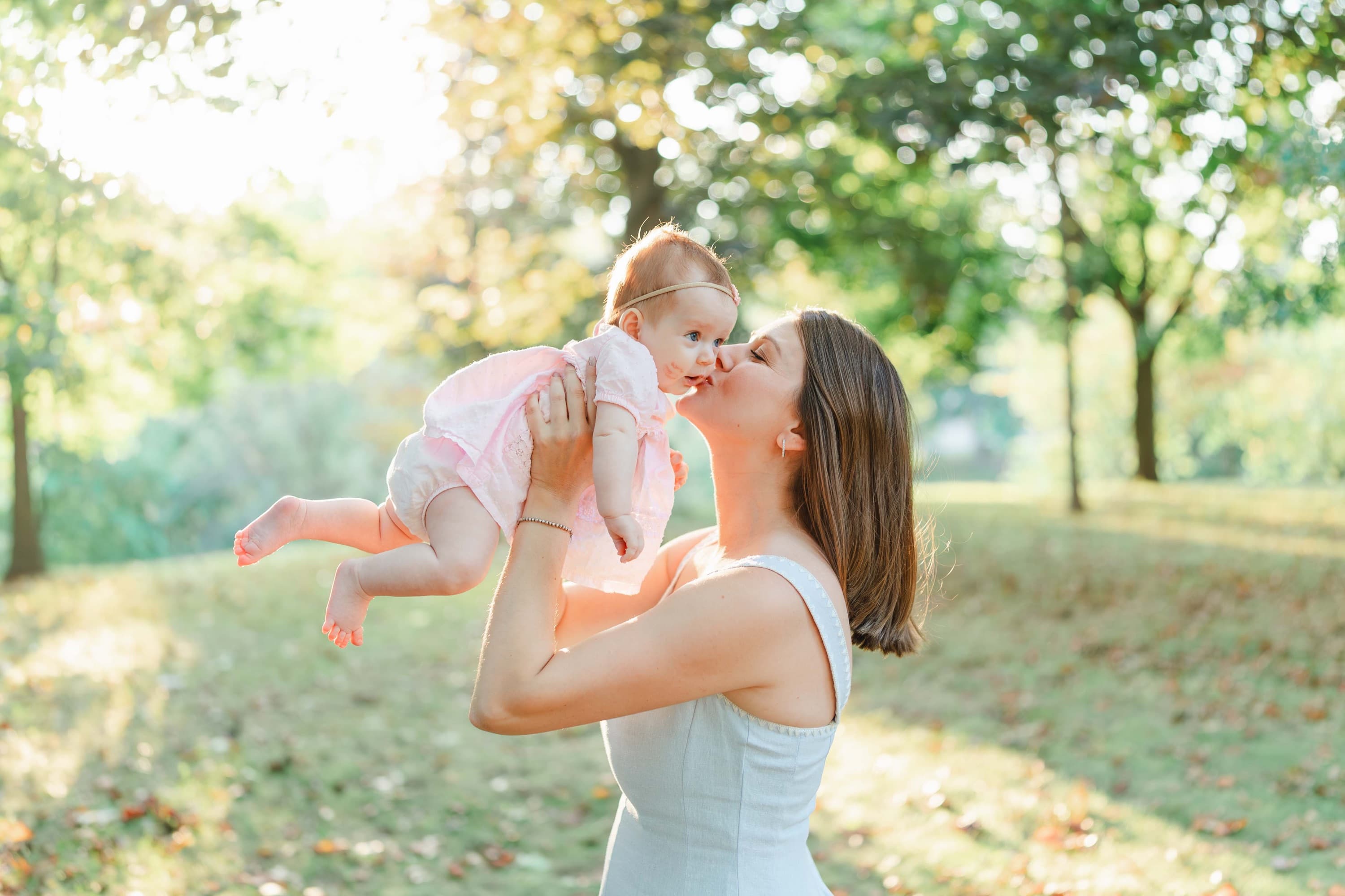 Mother holding up her daughter and kissing her during a golden hour family session in Grimsby Ontario.